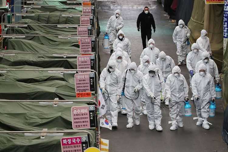 Para petugas dilengkapi pakaian pelindung menyemprotkan cairan desinfektan di sebuah pasar di daerah Daegu, Korea Selatan