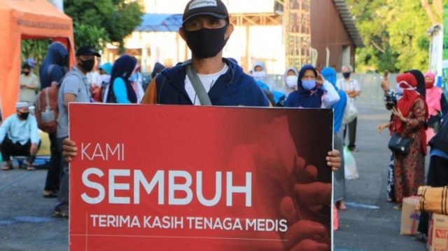 Seorang warga yang dinyatakan sembuh dari Covid-19 membawa spanduk bertuliskan ucapan terima kasih kepada tenaga medis saat dipulangkan dari tempat karantina di Asrama Haji Surabaya, Jumat (5/6/2020). (HUMAS PEMKOT SURABAYA) (Foto: Kompas.com)